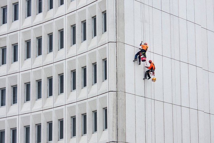 color in photography: two workers dressed in bright orange suspended from the side of a building