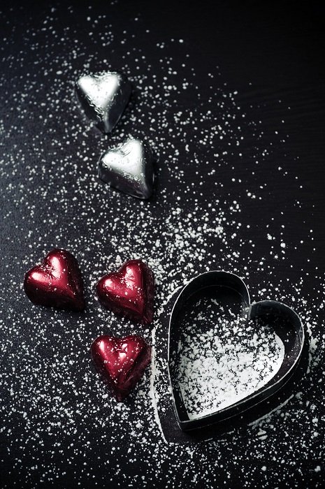 flat lay background idea: heart-shaped chocolates and cookie cutter sprinkled with confectionary sugar on the black background