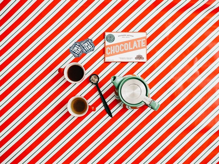 flat lay background idea: tea and chocolates on top of Christmas themed wrapping paper
