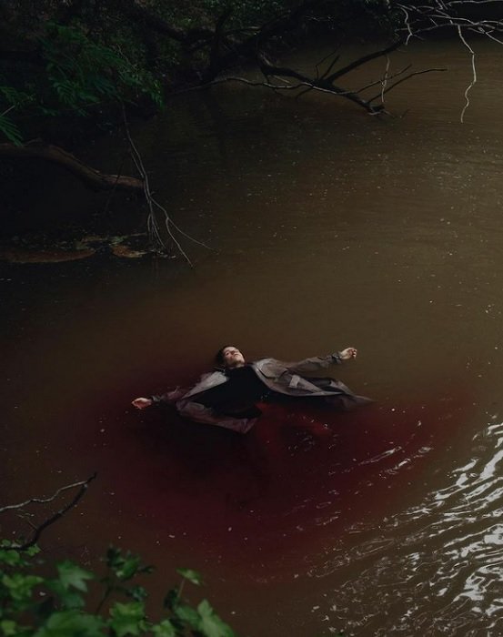horror photography: a dead body with outstretched arms rests along a river bank
