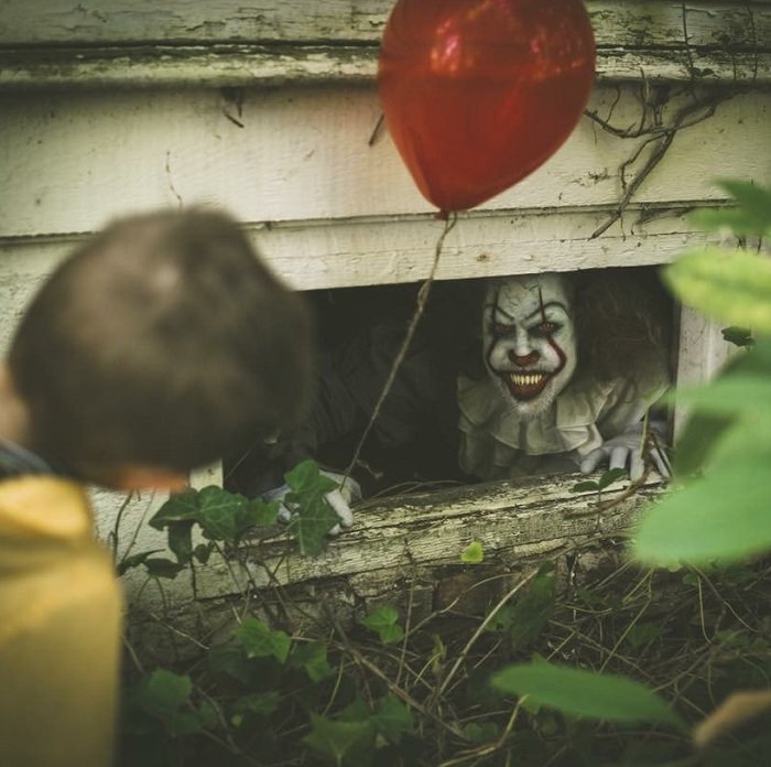 страшная фотография ужасов: Клоун Пеннивайз выглядывает из подвального окна на мальчика