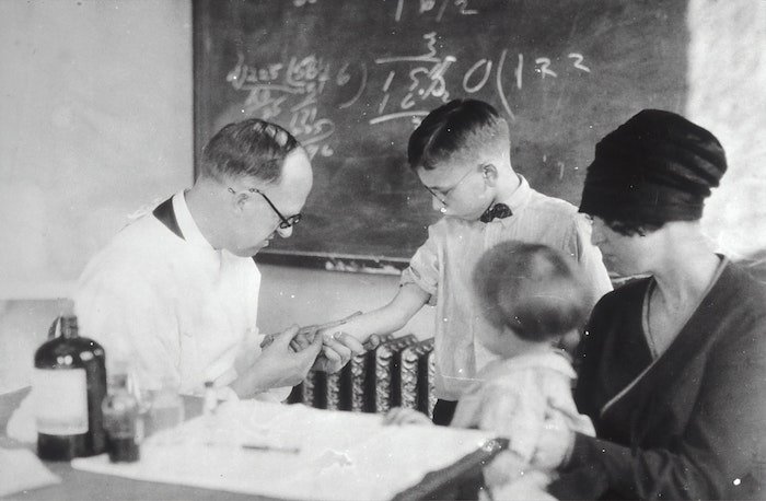 Медицинская фотография: Старое черно-белое изображение врача, обслуживающего маленького мальчика с семьей
