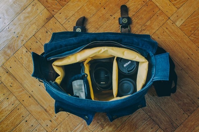 полная сумка для фотоаппарата, сидящая на деревянном полу
