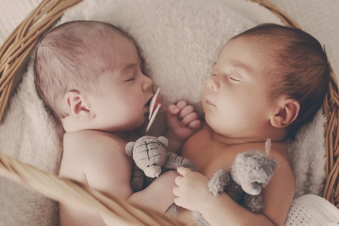 фотосессия новорожденных близнецов: новорожденные близнецы позируют лицом друг к другу в мягкой плетеной корзине