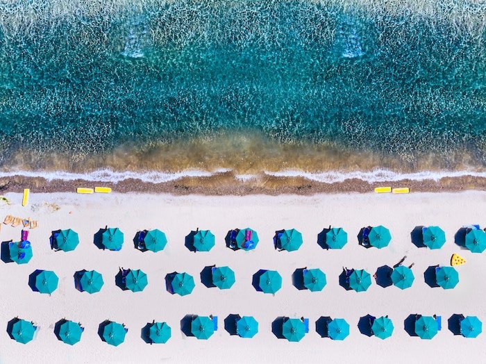 Повторение в фотографии: Аэрофотоснимок повторяющихся зонтиков на пляже и элементов океана