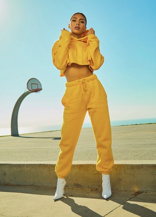 color block photoshoot ideas: a model in yellow sweat suit poses in front of the basketball court and a bright blue sky
