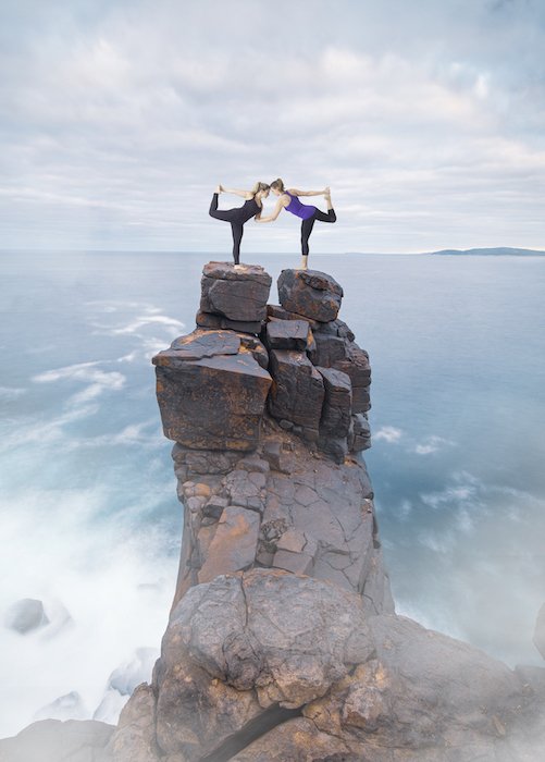 Композиционное фотоизображение женщин в позе йоги на вершине скалы у воды