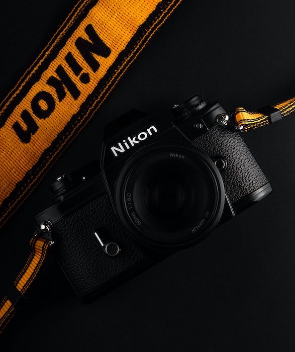 плоская фотография черной камеры Nikon с ярким оранжевым ремешком на черном фоне