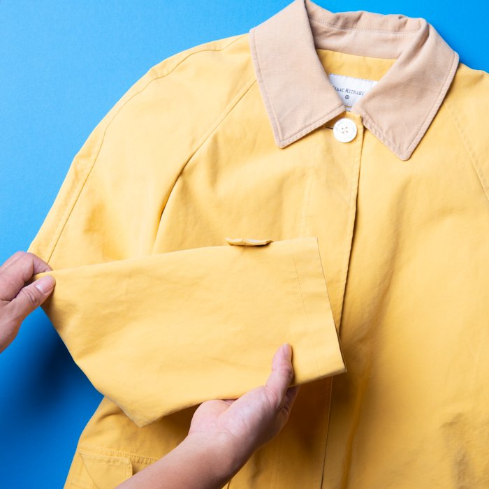 Flat Lay Photography of Clothing: Yellow coat being handled by the person for the clothing flat lay