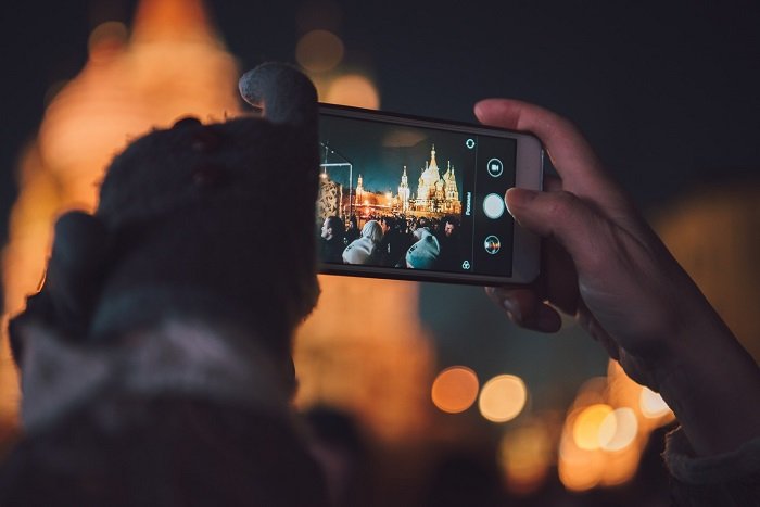 фотограф со смартфона снимает ночную сцену освещенных зданий
