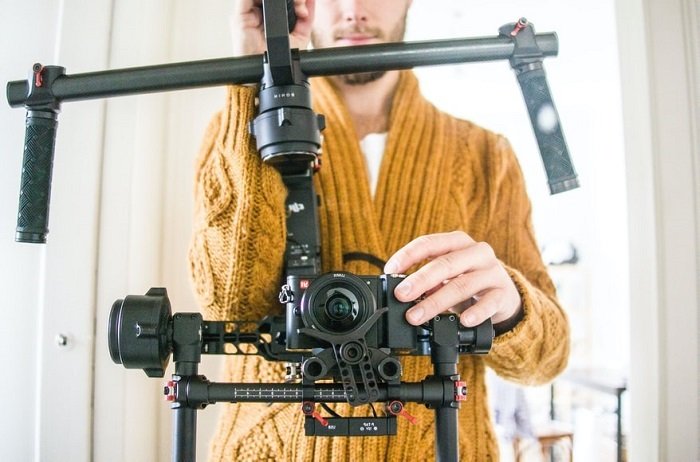 снимок головы видеографа в желтом свитере, использующего стабилизатор на своей зеркальной камере
