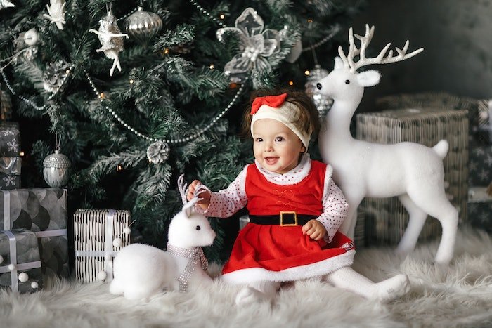 Ребенок в костюме Санты и со статуэтками оленей для рождественской открытки