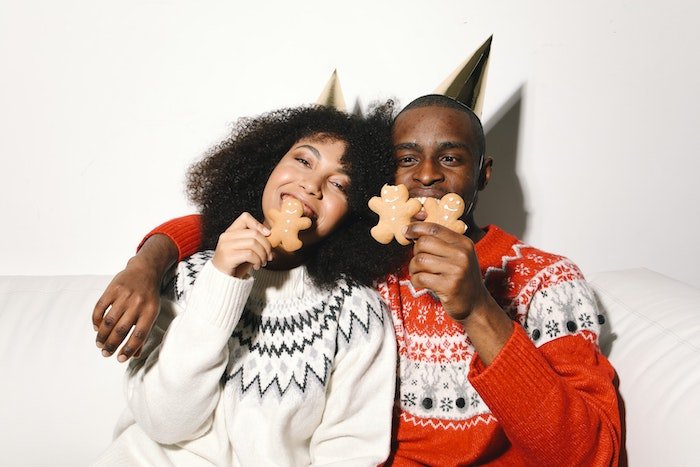 Пара в праздничных свитерах откусывает кусочек имбирного печенья для рождественской открытки фото идеи
