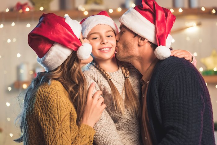 Ребенок, которого целуют родители в шапках Санта-Клауса для рождественской открытки фото идеи