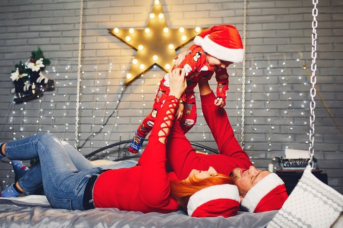 Советы для рождественской фотосессии пары: пара лежит на кровати, держа на руках своего ребенка в пижаме