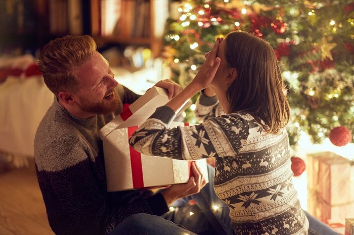 Идеи фотосессии рождественской пары: парень открывает коробку с подарком, а девушка закрывает глаза руками