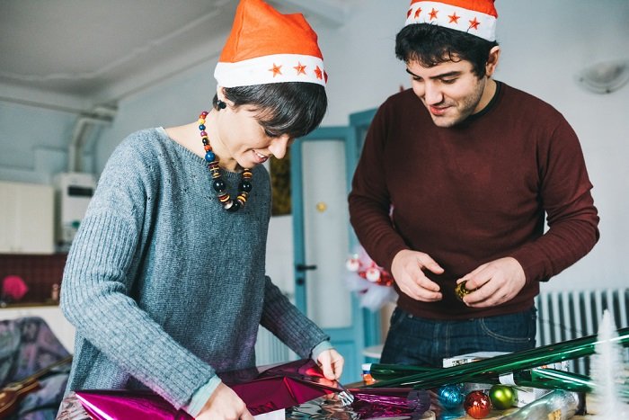 Советы по фотосессии рождественской пары: пара в шапках Санты вместе заворачивает рождественские подарки