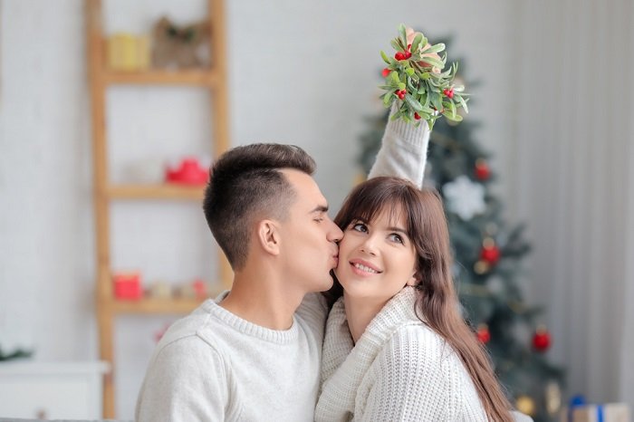 Советы для рождественской фотосессии пары: парень целует свою девушку в щеку под омелой