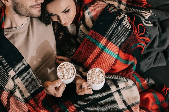 Советы по фотосессии рождественской пары: пара уютно устроилась рядом друг с другом, чтобы выпить горячего шоколада