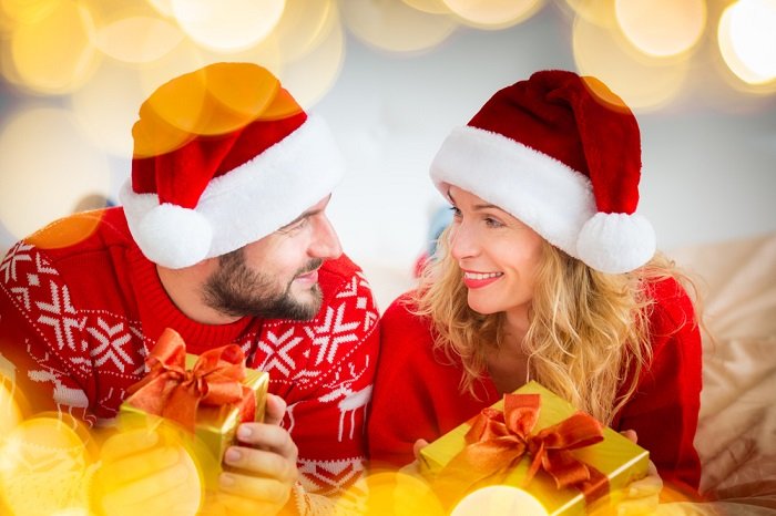 пара, сфотографированная в шапках Санты и рождественских свитерах, смотрит друг другу в глаза