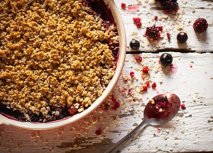 A berry crumble in the bowl agains a wood food photography prop background