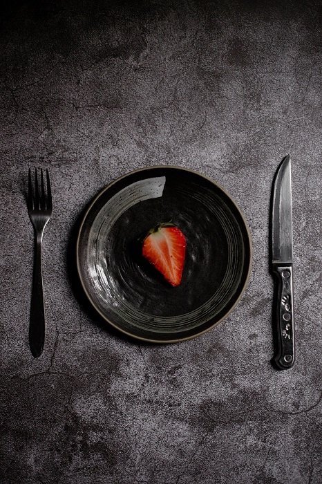 Нарезанная клубника на черной тарелке, с вилкой и ножом, используемая в качестве реквизита для фуд-фотографии
