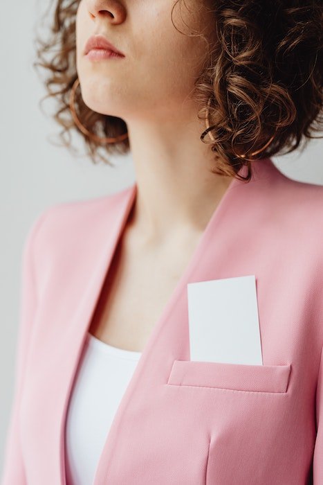 Визитные карточки в верхнем кармане женщины, которая одета в розовый пиджак. 