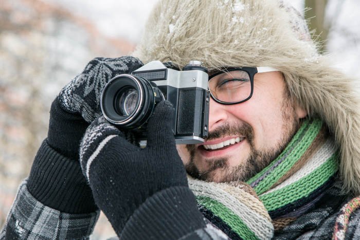 Мужчина в зимних перчатках и шапке делает снимок с фотоаппаратом