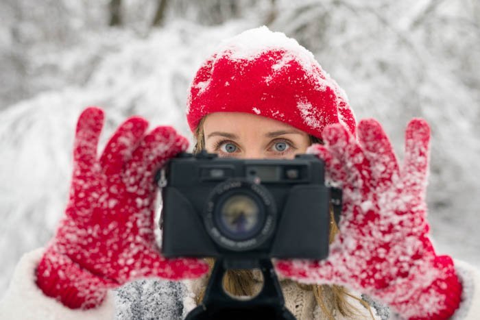 Женщина держит камеру в зимних перчатках