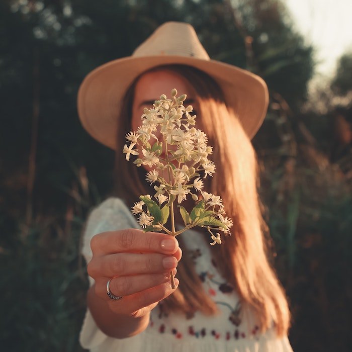 Портрет женщины в шляпе, держащей полевые цветы перед камерой, чтобы скрыть лицо