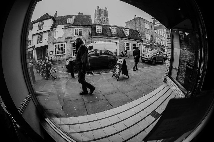 фотография человека, идущего по улице, увиденного через окно, сделанная объективом 