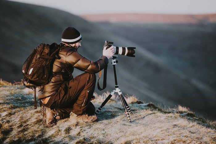 Ландшафтный фотограф делает снимок на хребте с зеркальной камерой и штативом