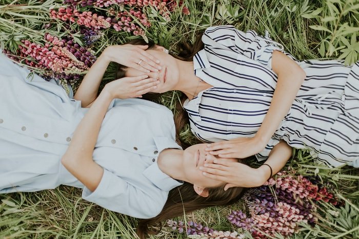 Две девушки лежат в поле, закрывая друг другу глаза