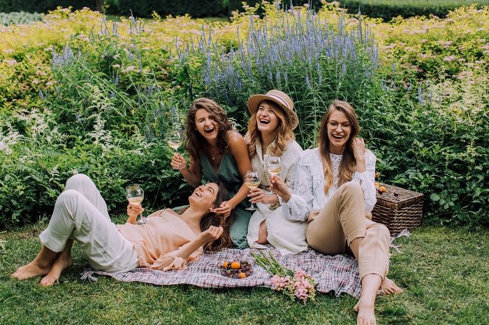 Четыре женщины устраивают пикник на лугу для фотосессии лучшей подруги