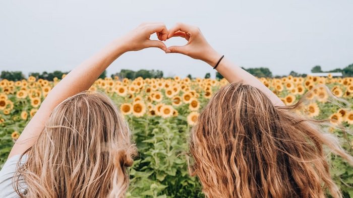 Две девушки в поле подсолнухов делают сердце из рук как идея для фотосессии лучших друзей