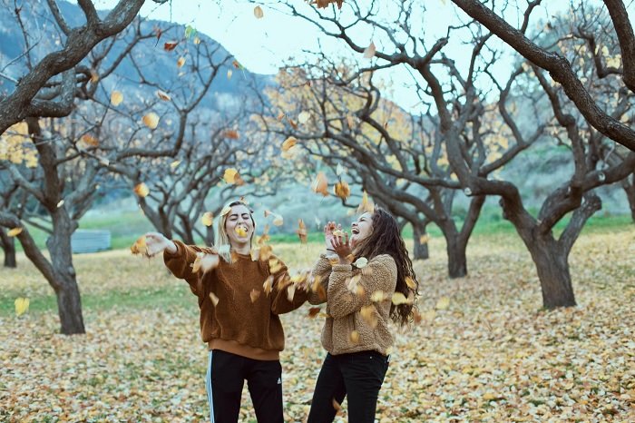 Две женщины бросают осенние листья в воздух