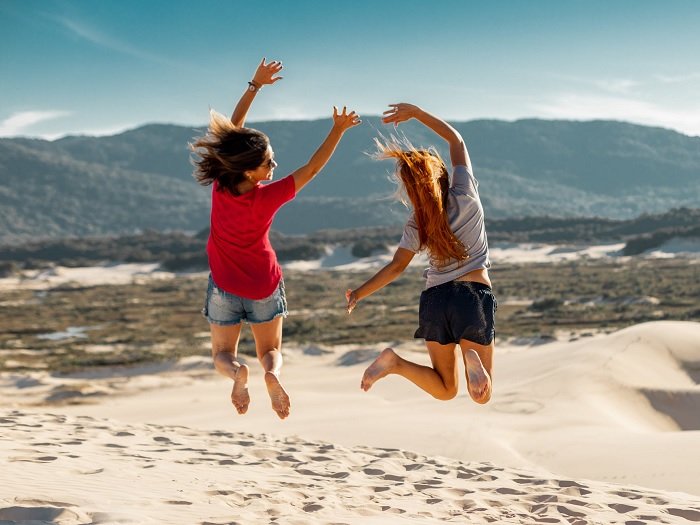 Две женщины прыгают по песчаной дюне