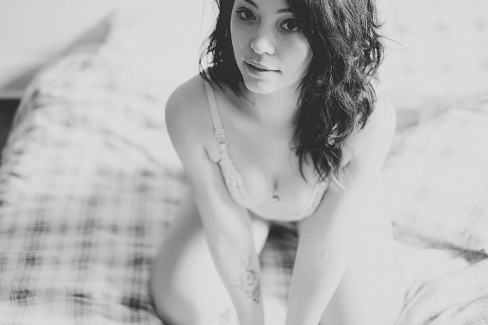 Черно-белая фотография женщины, стоящей на коленях на кровати для будуарной фотосессии