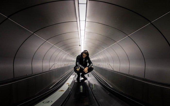 Мужчина приседает в подземном тоннеле с конвейерными лентами как идея для мужских поз
