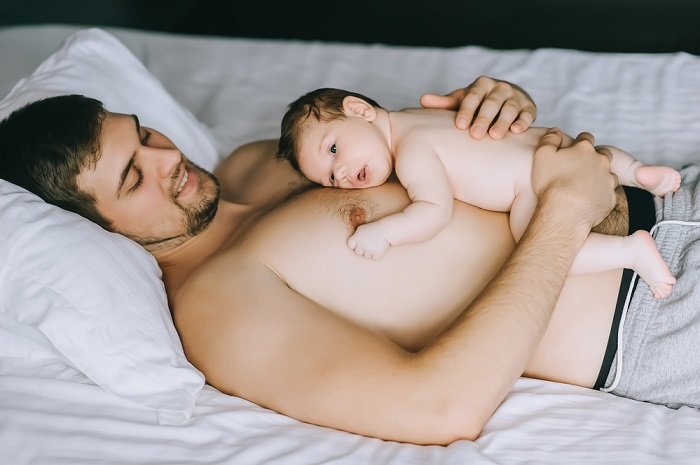 Ребенок лежит на груди отца на кровати как пример фото новорожденного