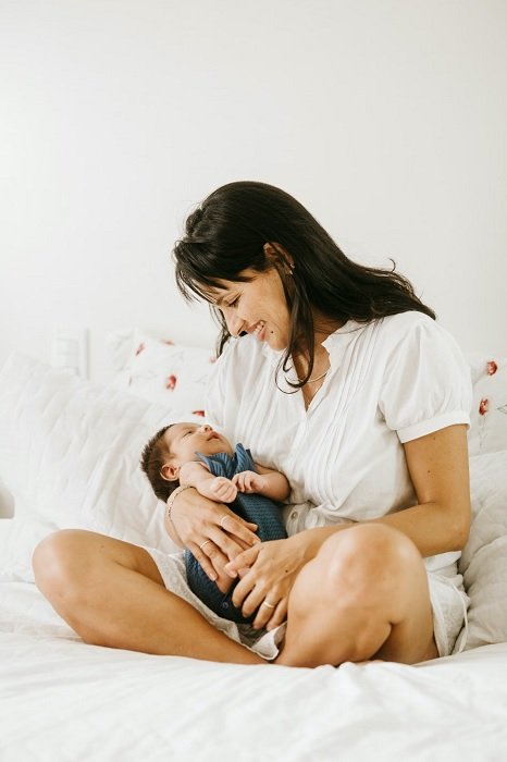 Мать, сидящая на кровати с младенцем на руках, как вдохновение для фотографии новорожденных