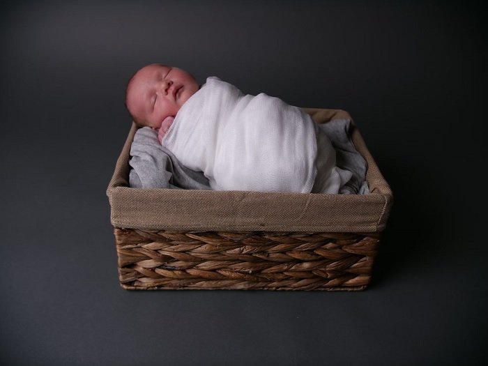Ребенок, завернутый в одеяло в корзине как идея для фото новорожденного