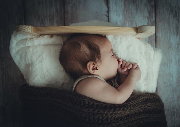 Малыш спит в миниатюрной кроватке для фотосессии новорожденных