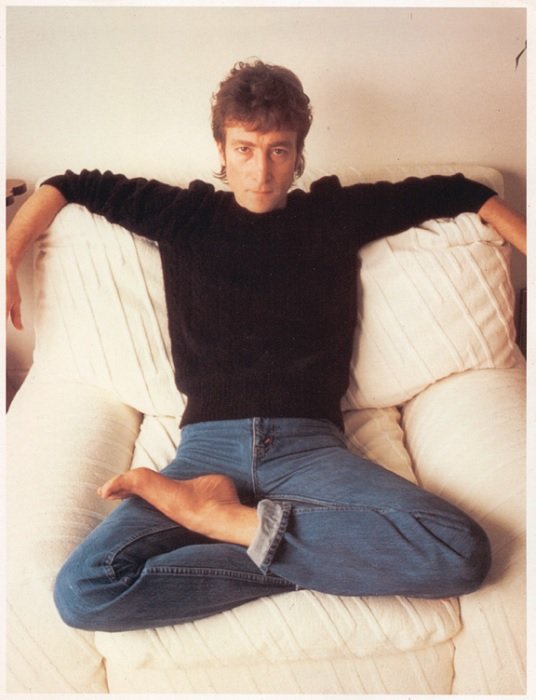 портрет Джона Леннона, сидящего со скрещенными ногами на белом диване
