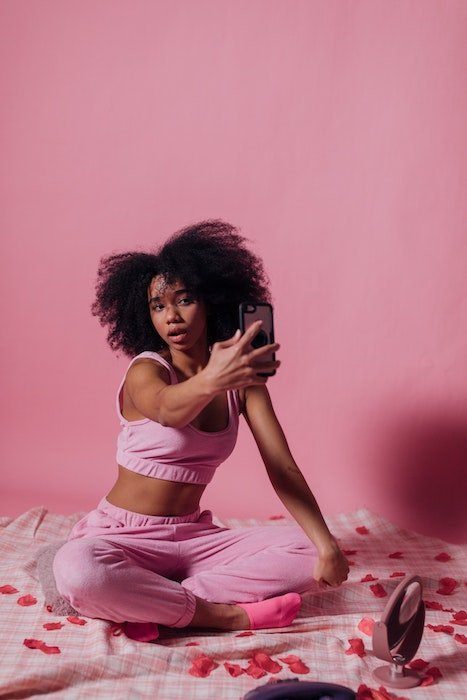 Женщина сидит на кровати в розовой комнате и делает селфи