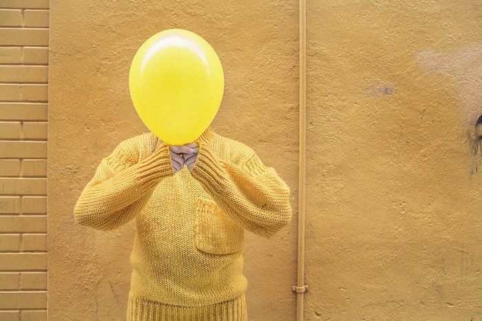 stock photo of the man in yellow jumper holding yellow balloon in front of his face
