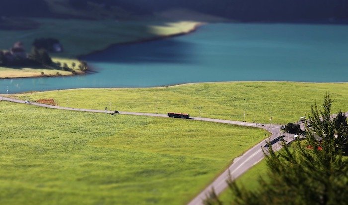 Миниатюрный снимок озера и поля, с крошечными машинками, едущими по дороге