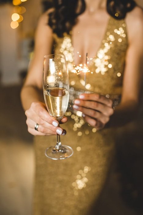 Женщина в золотом платье держит бокал шампанского и игристое