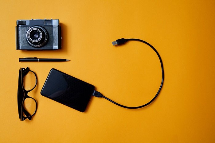 Камера, жесткий диск и очки на оранжевом фоне