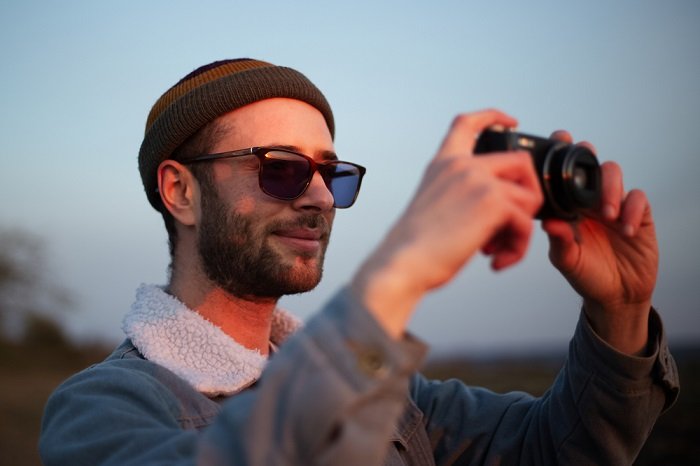 Человек в шерстяной шапке фотографируется с компактной камерой